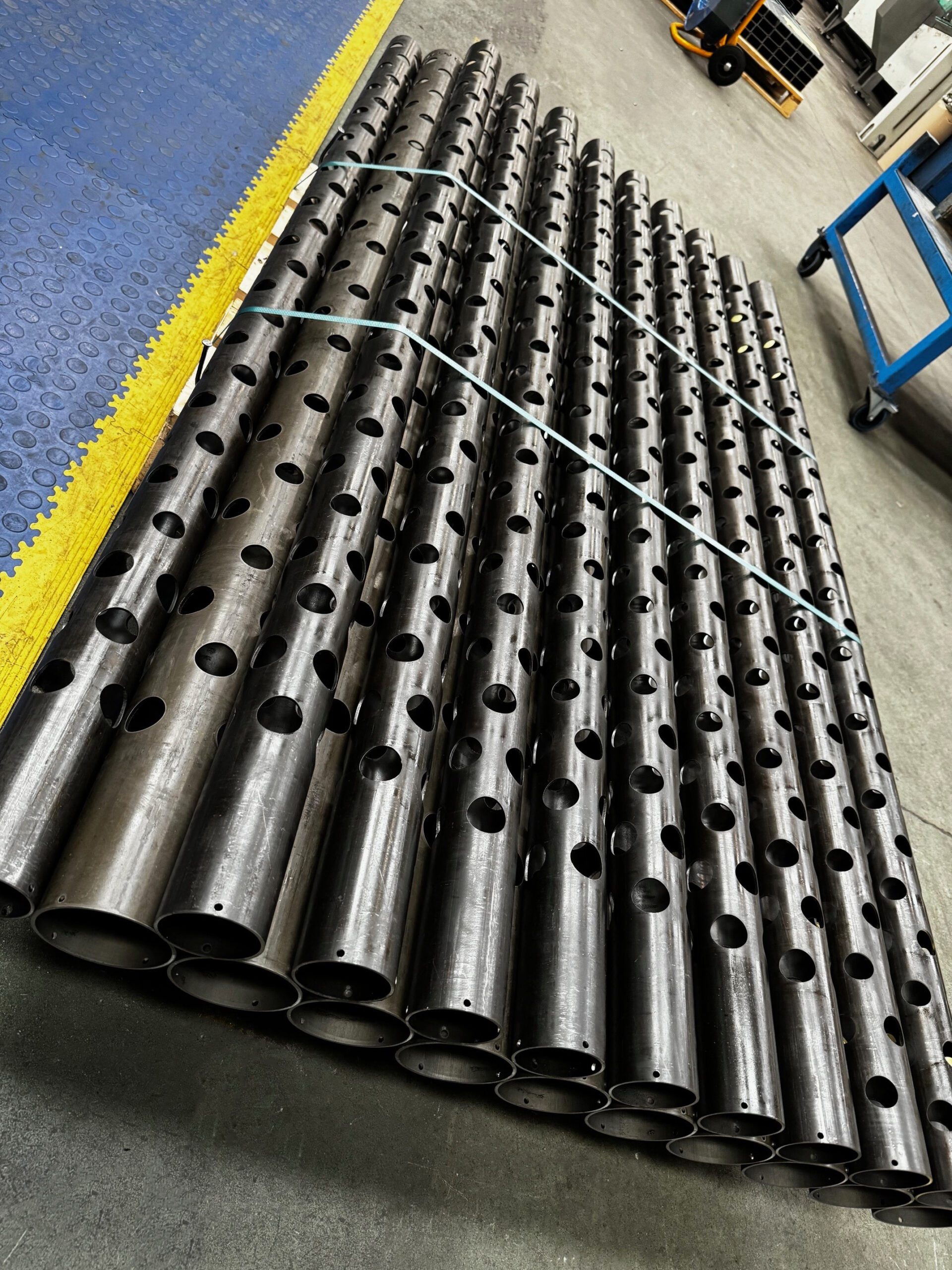 Tube cut parts with circular holes laser cut out, they are shown stacked on a pallet on the factory floor